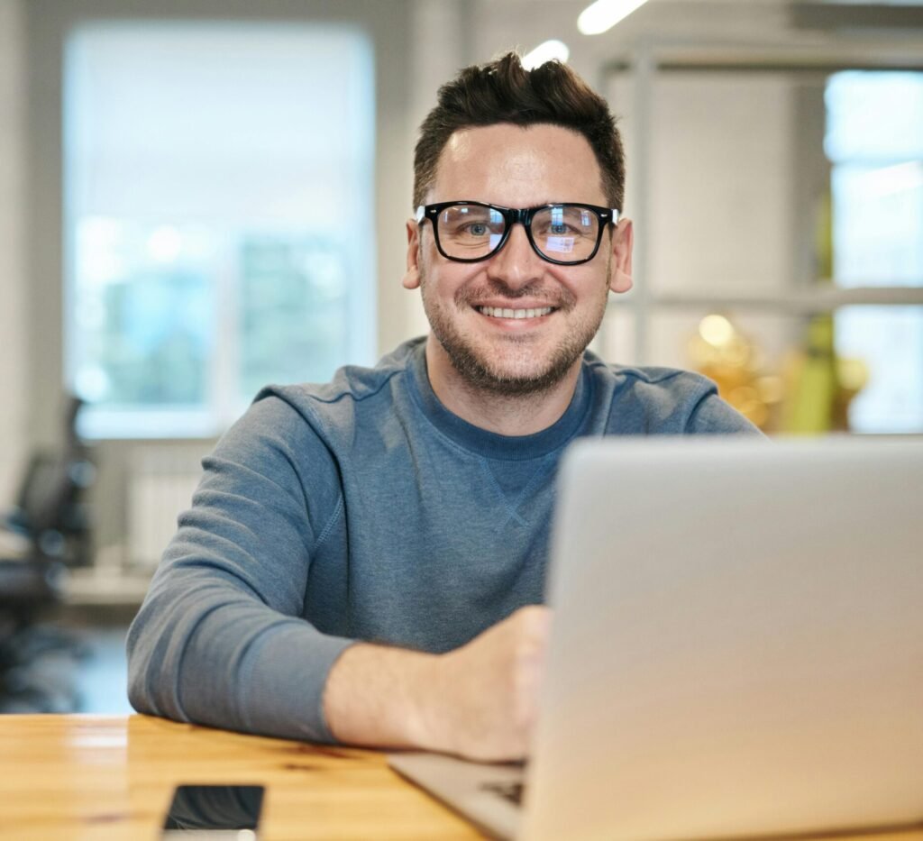 pexels-photo-3184611-3184611 Happy man wearing glasses working remotely on laptop in modern office environment.